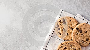 Freshly baked chocolate chip cookies on a kitchen towel, set against a minimalist grey background.