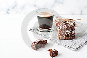 Freshly baked chocolate cookies and cup of coffee on gray napkin on wooden background.