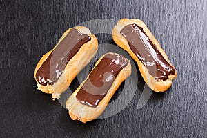 Freshly baked chocolate eclairs on black background.