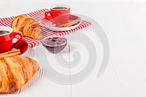 Freshly baked croissant on napkin, cup of coffee in red cup on white wooden background. French breakfast. Fresh pastries for break