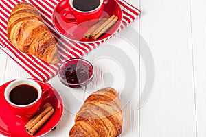 Freshly baked croissant on napkin, cup of coffee in red cup on white wooden background. French breakfast. Fresh pastries for break