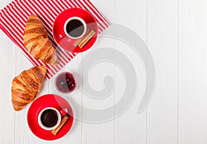 Freshly baked croissant on napkin, cup of coffee in red cup on white wooden background. French breakfast. Fresh pastries for break