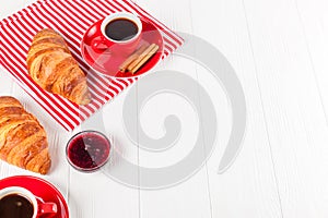 Freshly baked croissant on napkin, cup of coffee in red cup on white wooden background. French breakfast. Fresh pastries for break