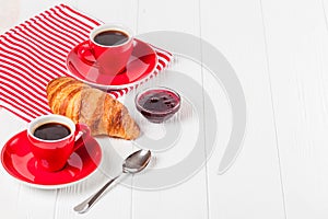 Freshly baked croissant on napkin, cup of coffee in red cup on white wooden background. French breakfast. Fresh pastries for break