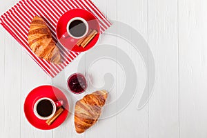 Freshly baked croissant on napkin, cup of coffee in red cup on white wooden background. French breakfast. Fresh pastries for break