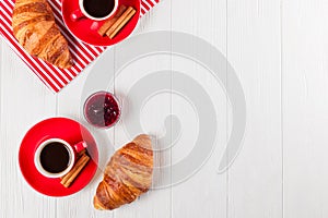 Freshly baked croissant on napkin, cup of coffee in red cup on white wooden background. French breakfast. Fresh pastries for break