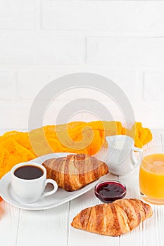 Freshly baked croissant orange juice, jam, cup of black coffee on white wooden background. French breakfast. Fresh pastries for mo