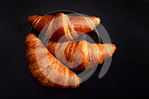 Freshly baked croissants in a black plate on a dark black background. Croissant cooking concept.