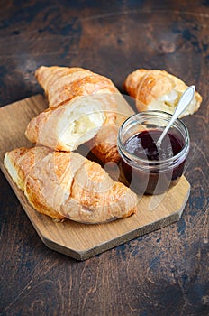 Freshly baked croissants with jam on dark wooden background.