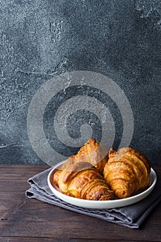 Freshly baked croissants on a plate, dark background, copy space