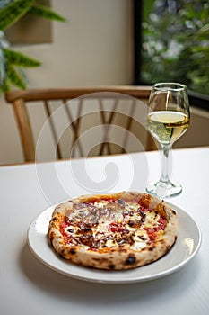 Freshly-baked delicious pizza with a glass of white wine on the table