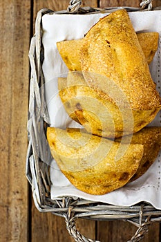 Freshly baked Empanadas Turnover Pies with vegetable cheese filling in tomato sauce in wicker basket. Plank wood background.