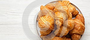 Freshly baked golden croissants on grey round plate on a white wooden background, overhead view. From above, top view, flat lay.
