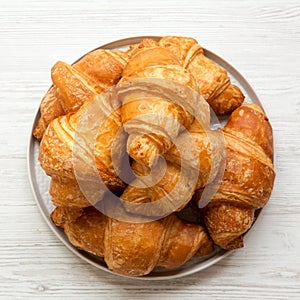 Freshly baked golden croissants on grey round plate on white wooden background, top view. From above, overhead, flat lay