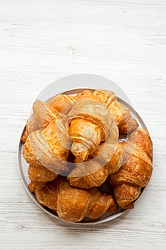 Freshly baked golden croissants on grey round plate on white wooden background, top view. From above, overhead.