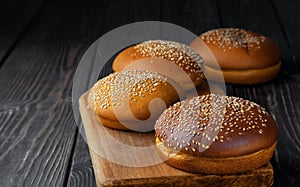 Freshly baked hamburger buns with sesame on dark wooden background. Round bun with sesame or bread rolls. Closeup