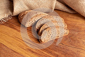 Freshly baked homemade bread with bran on a wooden background and burlap cut into slices. Foodphoto.