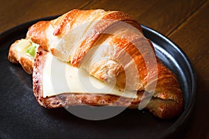 Freshly baked homemade delicious croissant sandwich ham cheese in black plate on wooden breakfast table