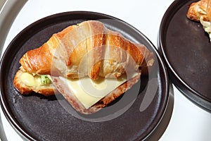 Freshly baked homemade delicious croissant sandwich ham cheese in black plate on wooden breakfast table, top view of breakfast