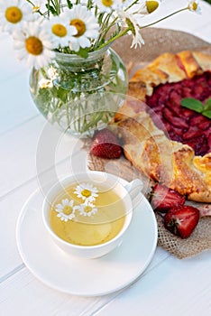 Freshly baked homemade galette or open strawberry pie and fresh mint leaves with a cup of chamomile herbal tea, summer food. Soft