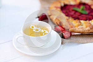 Freshly baked homemade galette or open strawberry pie and fresh mint leaves with a cup of chamomile herbal tea, summer food. Soft