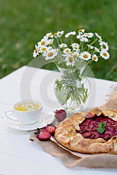 Freshly baked homemade galette or open strawberry pie and fresh mint leaves with a cup of chamomile herbal tea, summer food. Soft