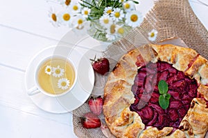 Freshly baked homemade galette or open strawberry pie and fresh mint leaves with a cup of chamomile herbal tea, summer food. Soft