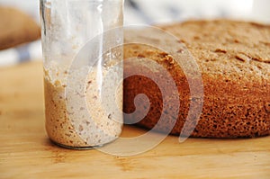 Freshly baked homemade rye-wheat whole grain bread and rye sourdough in a glass jar. Close up