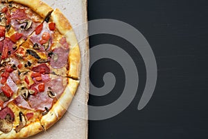 Freshly baked pizza in a cardboard box on dark background, top view. Closeup, copy space. Flat lay,