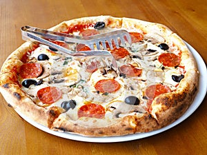 Freshly baked pizza with mushrooms, sausage and olives stands on a wooden table. Closeup photo