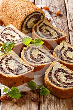 Freshly baked poppy roll with raisins, decorated with mint close-up on a table. vertical
