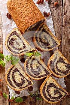 Freshly baked poppy roll with raisins, decorated with mint close-up on a table. Vertical top view