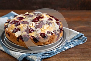 Freshly baked small cherry cake with almond slivers, rustic wood and dark background with copy space