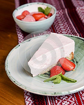 Freshly baked strawberry cheesecake with fresh strawberries and mint. Served on a plate.