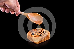 Freshly baked sweet bun with raisins, cinnamon and sweet glaze isolated on black background. Homemade traditional bakery