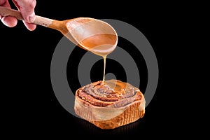 Freshly baked sweet bun with raisins, cinnamon and sweet glaze isolated on black background. Homemade traditional bakery