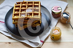 Freshly baked sweet delicious appetizing Belgian waffles with honey on a black plate on a wooden table.