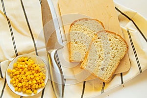 Freshly baked traditional wheat bread, corn grains and knife on linen kitchen towel, flat lay