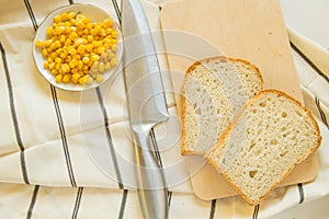 Freshly baked traditional wheat bread, corn grains and knife on linen kitchen towel, flat lay