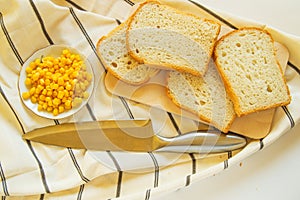 Freshly baked traditional wheat bread, corn grains and knife on linen kitchen towel, flat lay