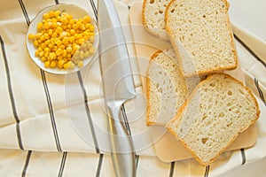 Freshly baked traditional wheat bread, corn grains and knife on linen kitchen towel, flat lay