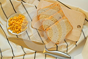 Freshly baked traditional wheat bread, corn grains and knife on linen kitchen towel, flat lay