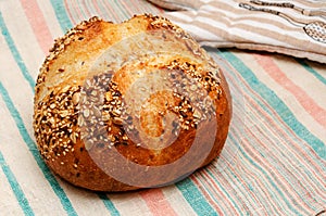 Freshly baked whole grain loaf of bread sprinkled with seeds of flax, sesame, sunflower seeds on linen towel. Closeup