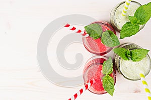 Freshly blended green and red fruit smoothie close up in glass jars with straw, mint leafs, top view. White wooden board backgroun