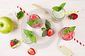 Freshly blended green and red fruit smoothie close up in glass jars with straw, mint leafs, top view. White wooden board backgroun