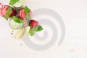 Freshly blended green and red fruit smoothie in glass jars with straw, mint leafs, top view.