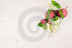 Freshly blended green and red fruit smoothie of strawberry and apple in glass jars with straw, mint leafs, top view.