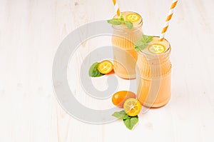 Freshly blended orange citrus kumquat fruit smoothie in glass jars with straw, mint leaf, cute ripe berry, copy space.