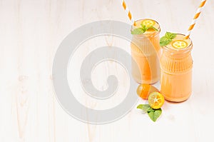 Freshly blended orange citrus kumquat fruit smoothie in glass jars with straw, mint leaf, cute ripe berry, copy space.