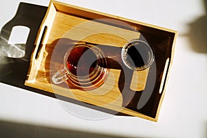 Freshly brewed black filter coffee is served on a bamboo tray on sunlit white table. Top view